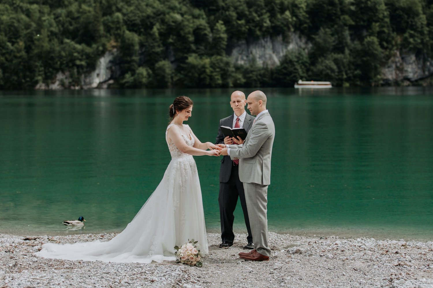 A couple stand holding hands during their wedding vows, the bright greenish blue waters of the Königsee in Berchtesgaden, Germany behind them