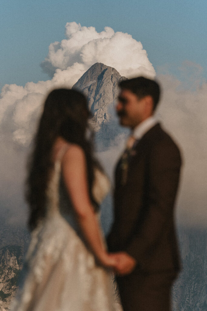 A couple stands holding hands with a grey, rocky mountain summit in focus behind them during their Slovenia elopement