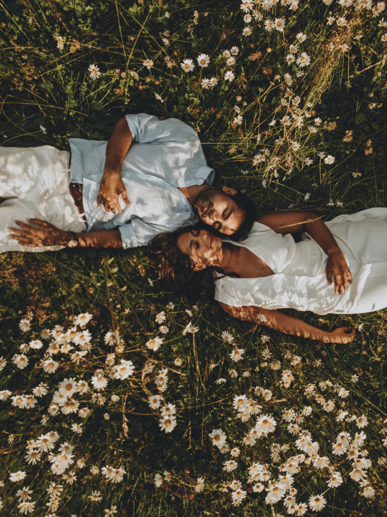 A couple lay head to head in a field of white daisies during their proposal shoot in the Dolomites