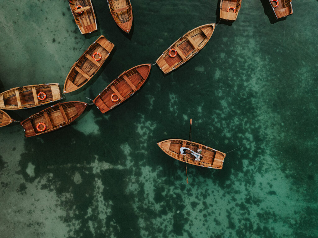 A couple is scene from above paddling a wooden boat on a blue green lake location in the European Alps