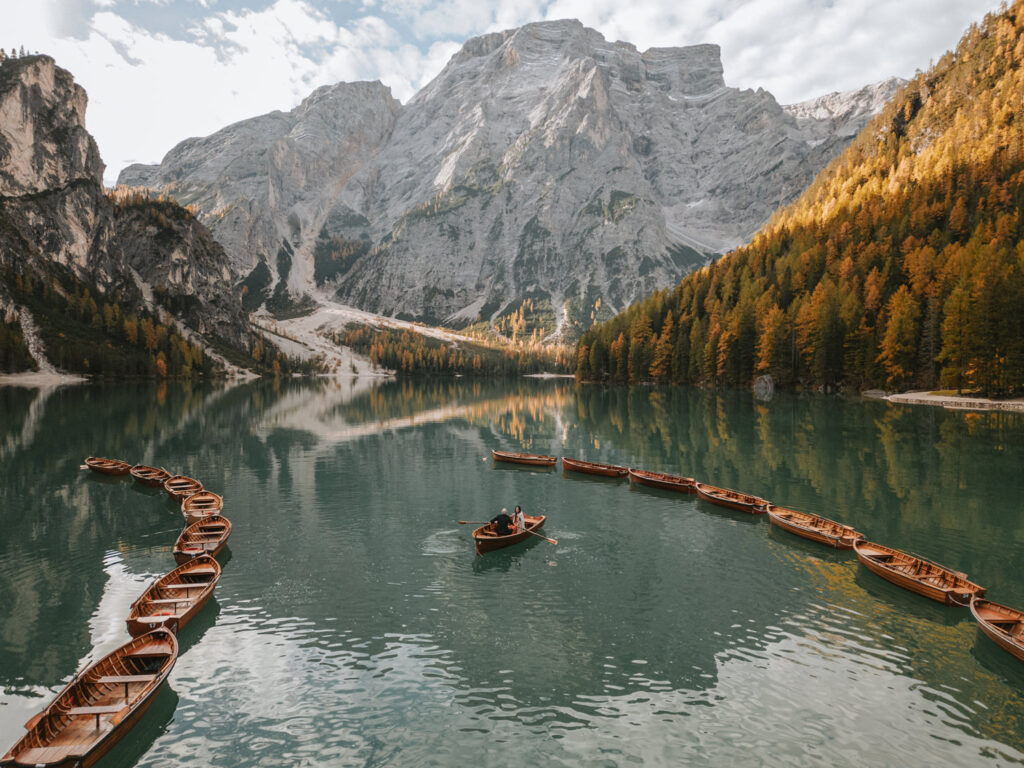 An elopement couple row a boat on a lake with vibrant October fall colors and a tall mountain behind them