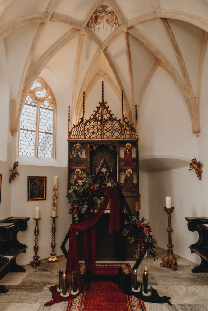 A gothic arch is set up in a medieval chapel at a Castle in Austria, surrounded by candles and flowers.