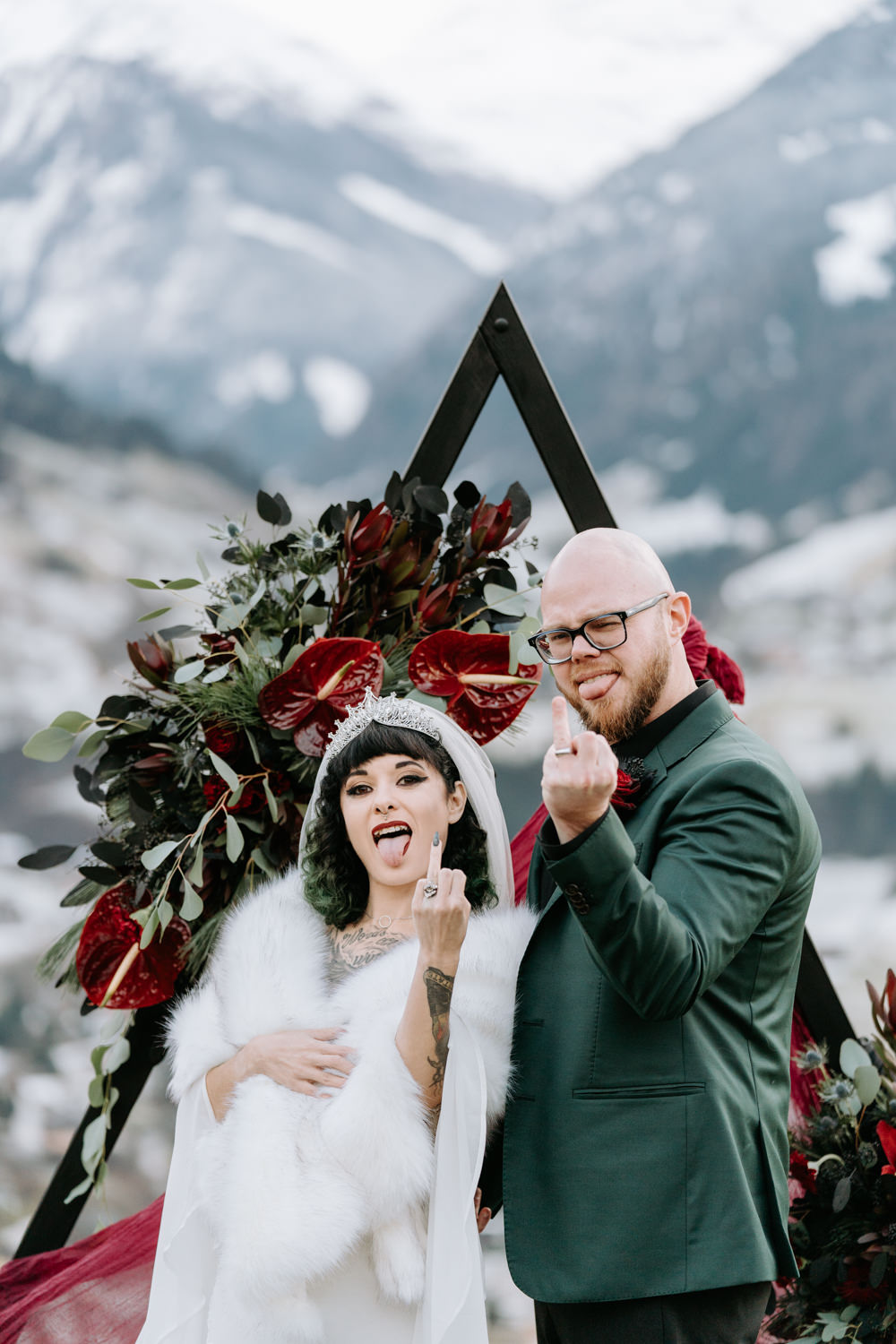 A gothic couple hold their middle ring fingers up to the camera posing for their wedding photos in Austria