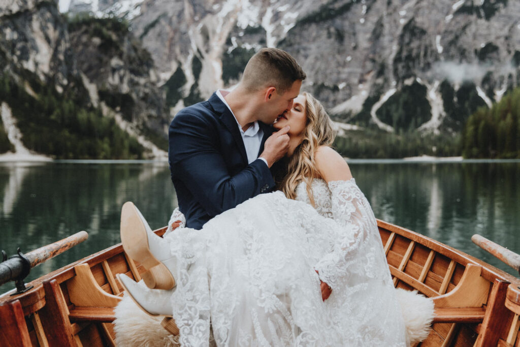 A couple kiss romantically on a wooden boat in the Dolomites during their rainy June elopement