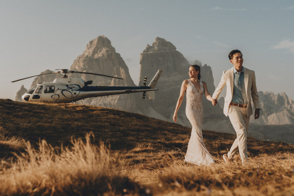 A couple walk away hand in hand from a helicopter, parked in front of the Tre Cime di Lavaredo, the most famous elopement location in the Dolomites