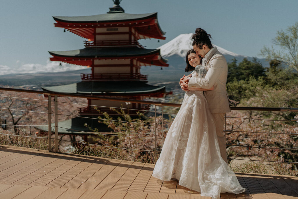 A couple in wedding clothes stand outside the Chureito Pagoda with a snow capped Mt. Fuji in the distance on their Japan elopement day