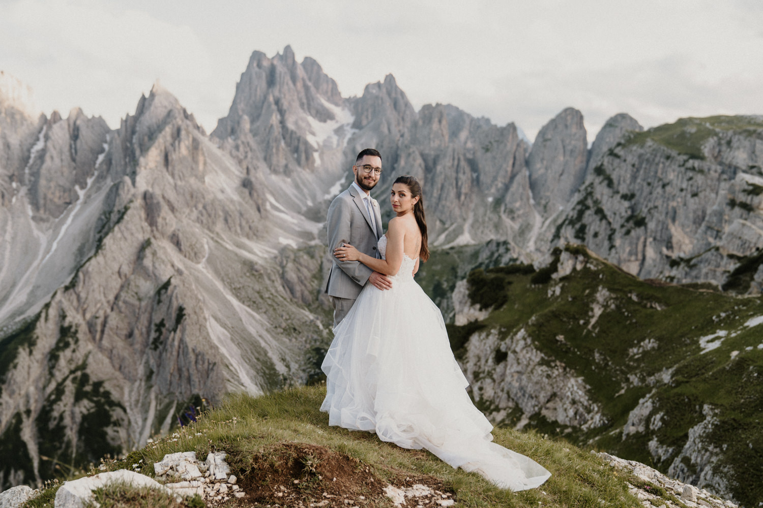 A couple in wedding dress and grey suit pose with the famous Cadini di Misurina mountain peaks behind them