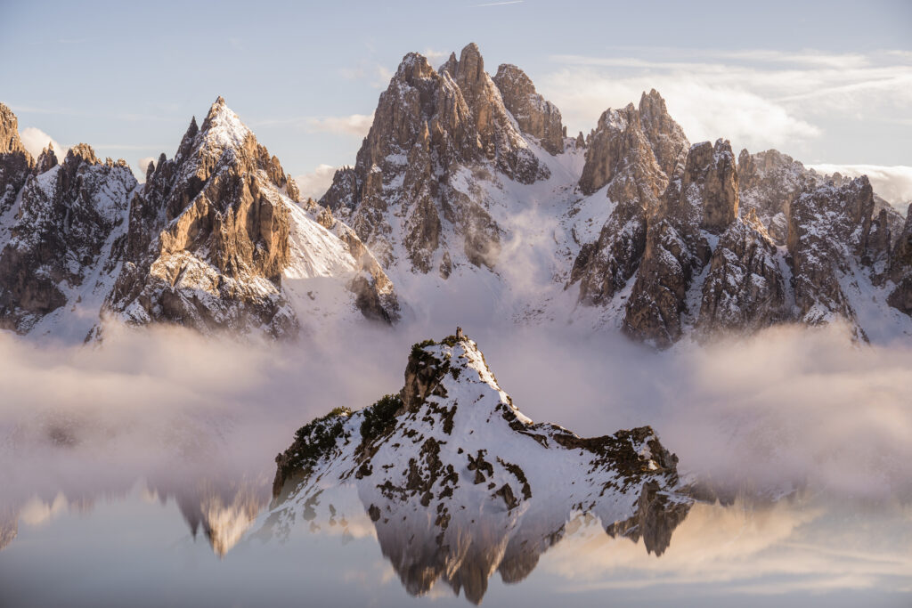 A couple stands far in the distance atop the Cadini di Misurina trail in the Italian Alps, surrounded by fog and snow