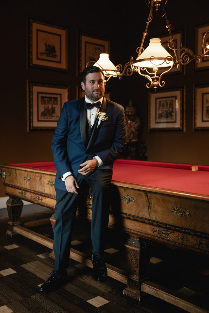 A man sits on a red pool table in the pool room of Grand Hotel Tremezzo, posing for his wedding photos on his elopement day