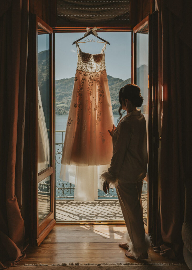 A bride in silhouette admires her wedding dress as it hands in the door frame of a room at the Grand Hotel Tremezzo on her elopement day