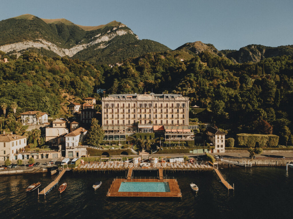 A drone photo of Grand Hotel Tremezzo as an elopement location on a sunny July Morning, with blue skies and a clear view of their floating pool and orange umbrellas.