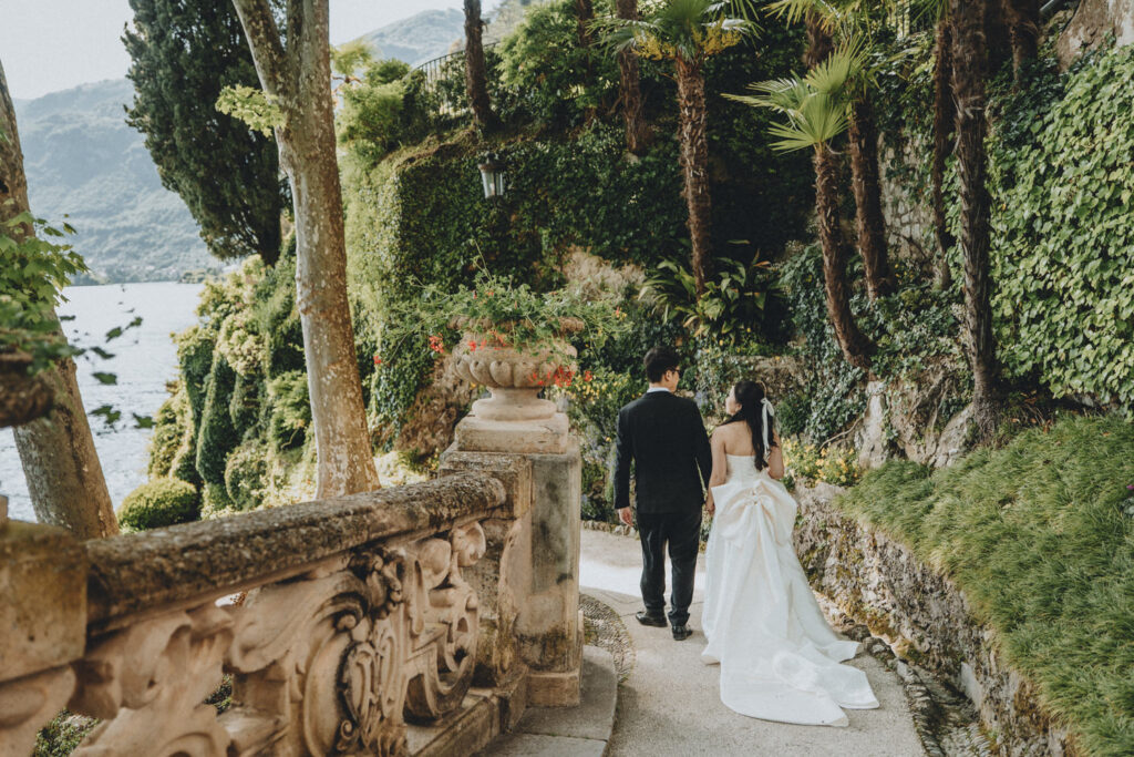 A couple in wedding attire walk on the stone paths of Villa del Balbianello's gardens