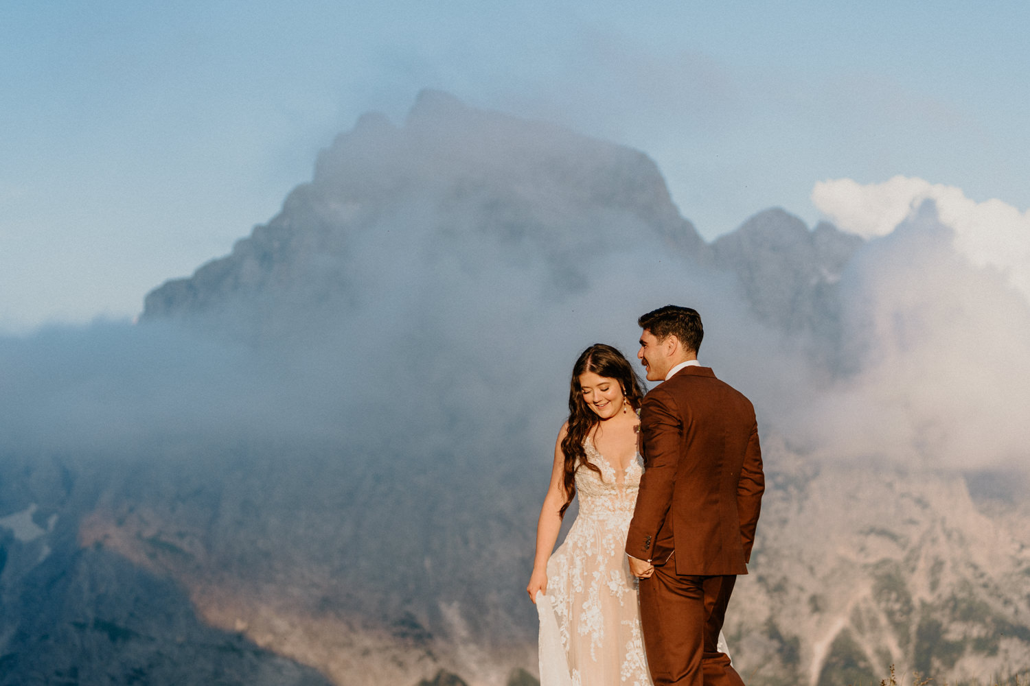 A couple in wedding attire stand lit by golden sunlight with tall mountains in the background on their Slovenia elopement day