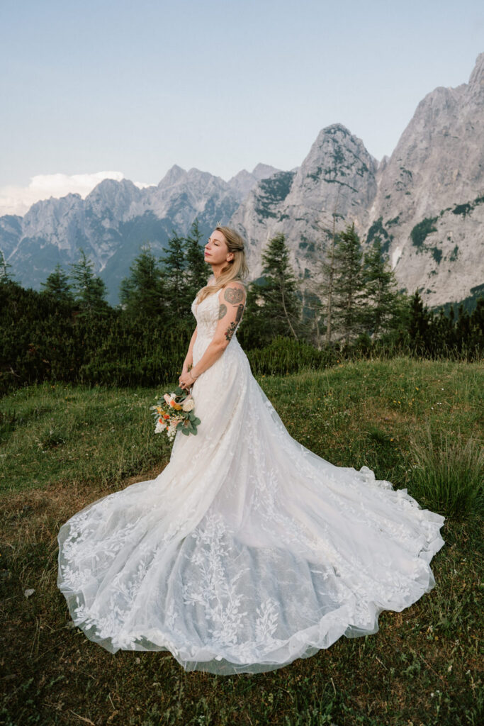A woman stands with her eyes closed on a tall mountain pass in Slovenia, posing for wedding photos on her elopement day