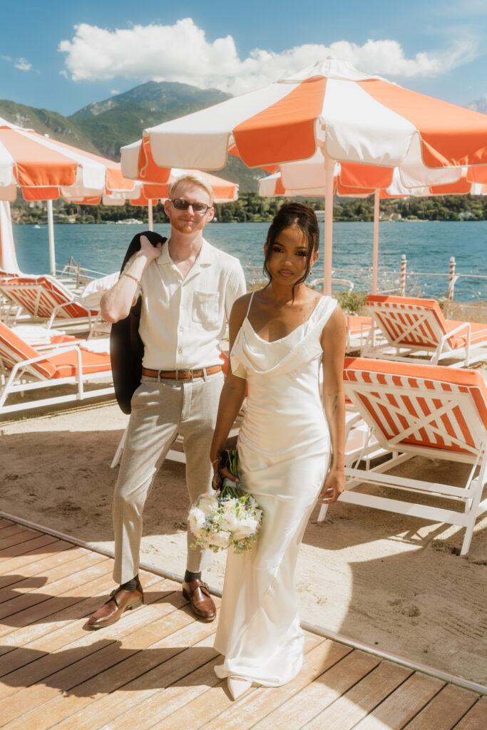 A couple poses dramatically for the camera under the iconic orange umbrellas of Grand Hotel Tremezzo, a popular wedding location along Lake Como.